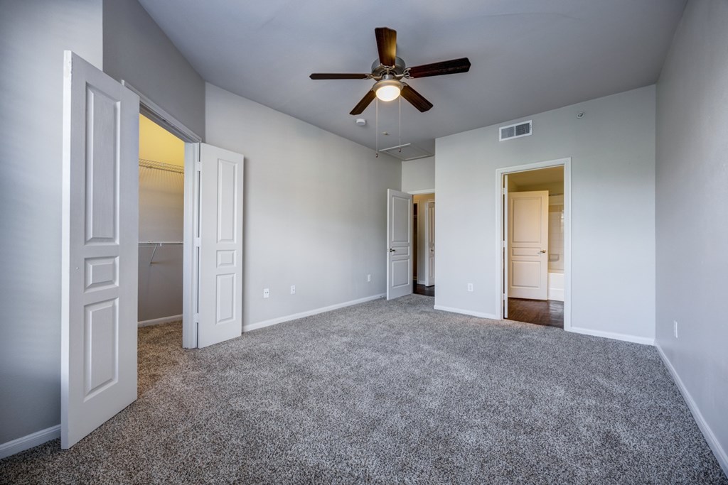 A spacious bedroom with a ceiling fan and carpeted floor.
