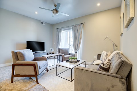 A living room with a grey couch, a wooden chair, a black television and a fan.