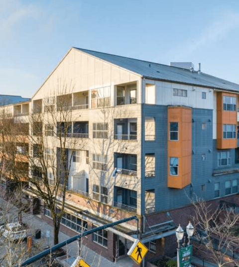 A pedestrian crossing sign is on a street in front of a multi-story building.