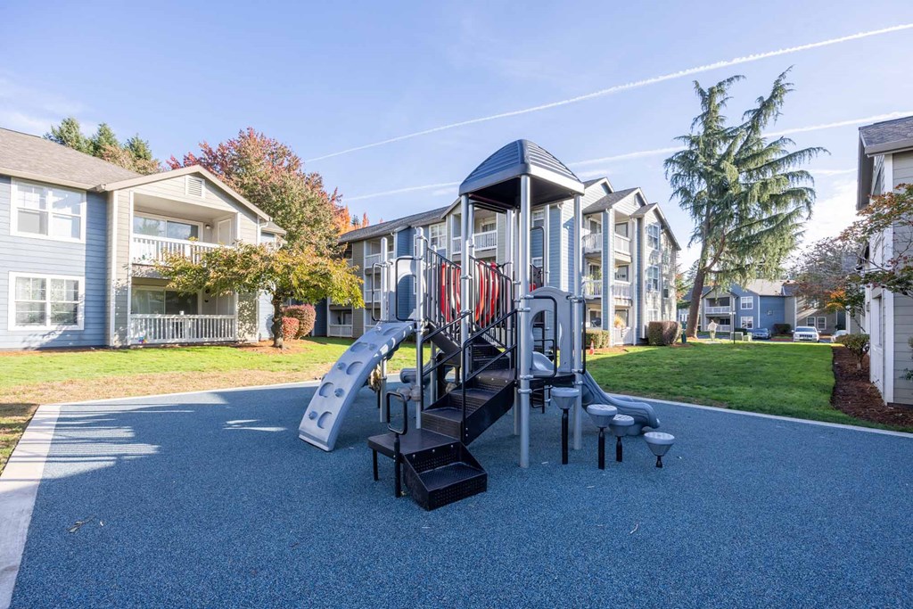 A playground with a slide and apartments in the background..