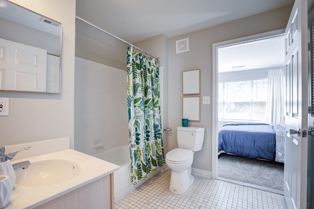 a bathroom with a shower, toilet and sink and a bedroom with a bed