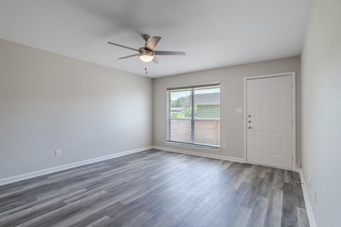 an empty living room with a ceiling fan and a window