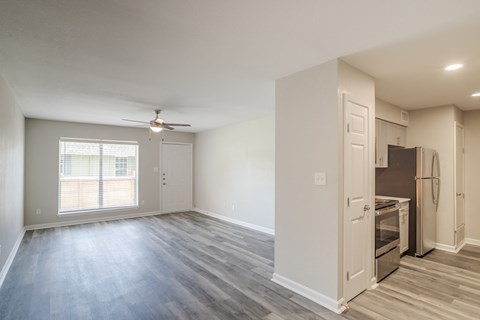 an empty living room with a kitchen and a ceiling fan