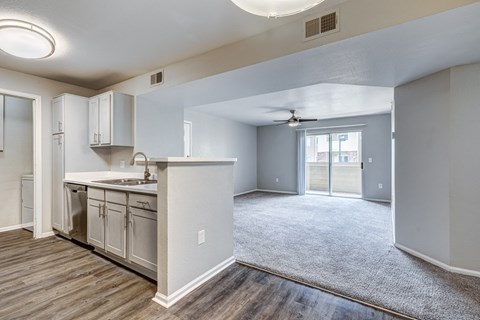 an empty living room with a kitchen and a ceiling fan
