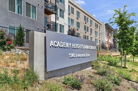 A concrete sign that says Academy Heights Apartments stands in front of a building.
