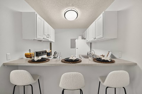 A kitchen with a counter and three chairs.
