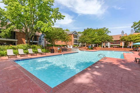 A large swimming pool surrounded by a brick patio and lounge chairs.