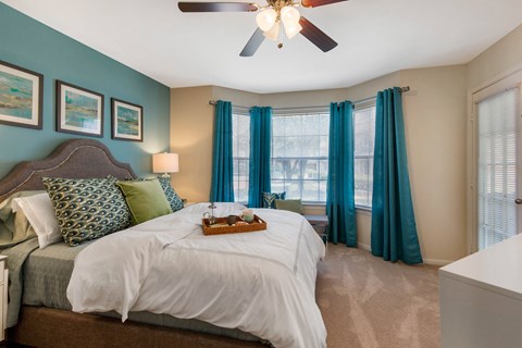 A bedroom with a bed, a ceiling fan, and a window with blue curtains.