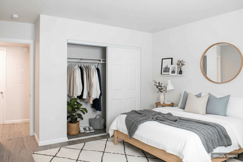A bedroom with a bed, a mirror, a plant, and a wardrobe.