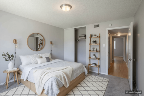 A bedroom with a bed, a mirror, and a small table with a plant on it.
