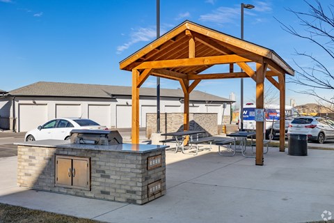 A wooden pavilion is situated in a parking lot with a stone pillar and a car parked in front.
