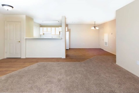 an empty living room and kitchen with a hard wood floor and carpet