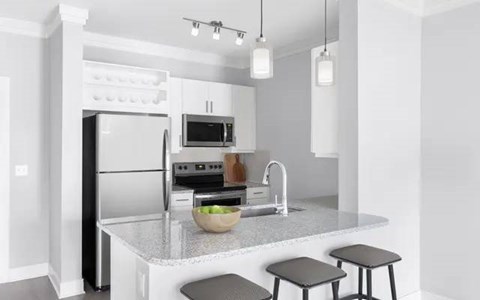 A modern kitchen with a refrigerator, microwave, oven, sink, and bar stools.