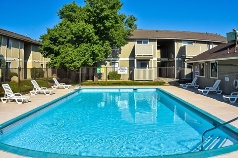 A swimming pool in front of apartment buildings with sun loungers around it.
