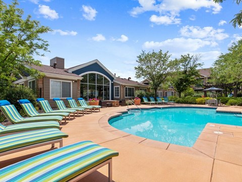 A pool surrounded by lounge chairs and a house in the background.