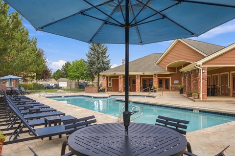 A poolside table with a blue umbrella is in the foreground of a residential area.