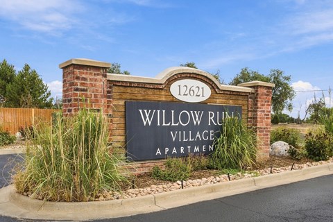 A sign for Willow Run Village Apartments is displayed in front of a brick wall.
