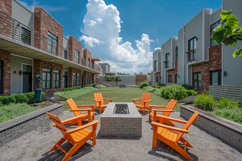 A row of orange chairs are arranged in a circle around a fire pit.