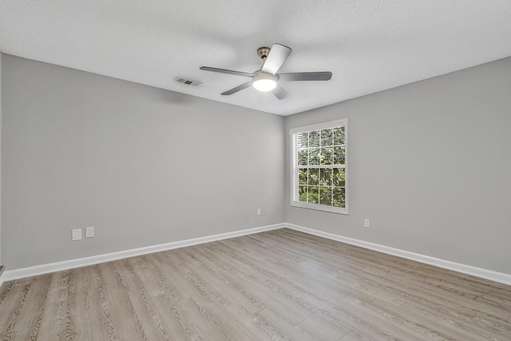 A room with a ceiling fan and a window showing greenery outside.