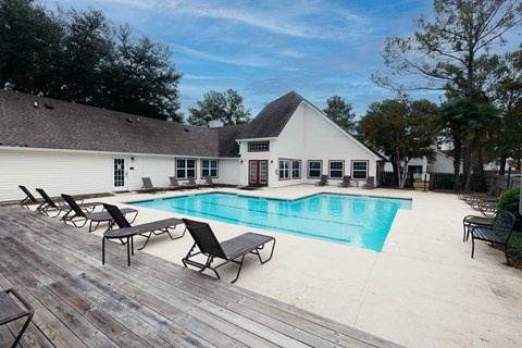 a swimming pool with chairs and a house in the background