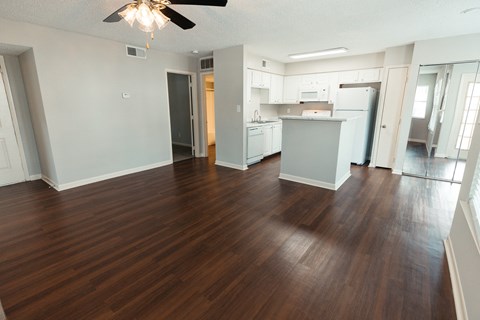 an empty living room and kitchen with wood flooring and a ceiling fan