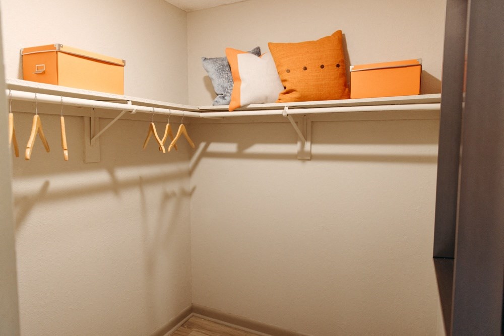 a walk in closet with a shelf with pillows and hangers