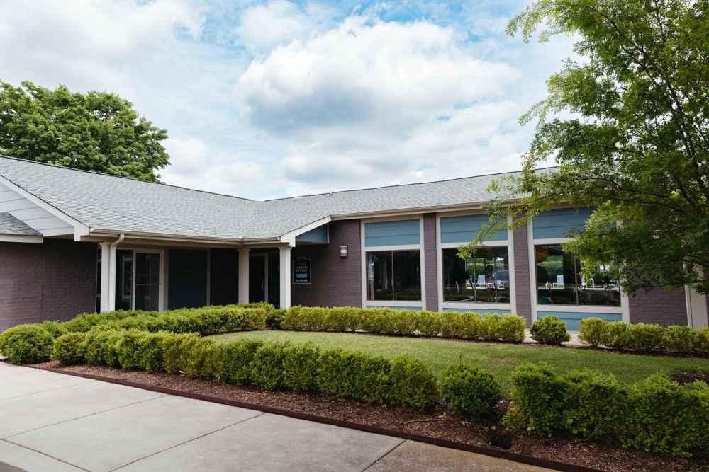 the front of a brick building with a sidewalk and landscaping