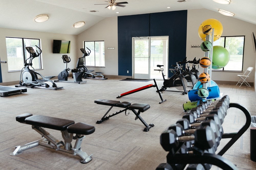 a gym with weights and other exercise equipment in a building with windows