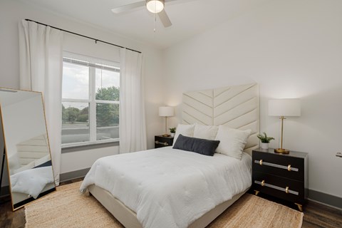 A bedroom with a large bed, a dresser, and a window with white curtains.