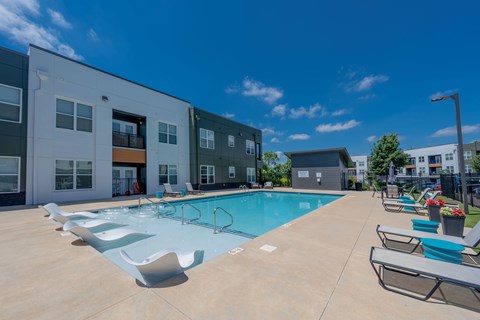 A swimming pool surrounded by sun loungers in front of a building.