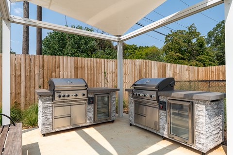 Two outdoor grills are built into stone bases under a white canopy.