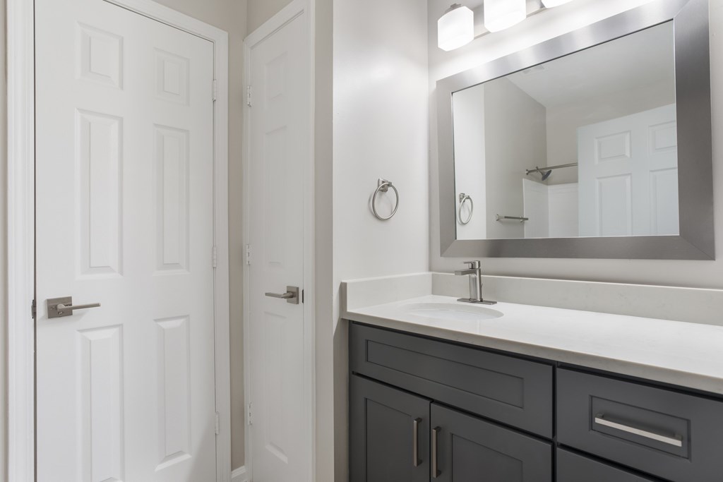 A bathroom with a white door, a mirror, and a sink.