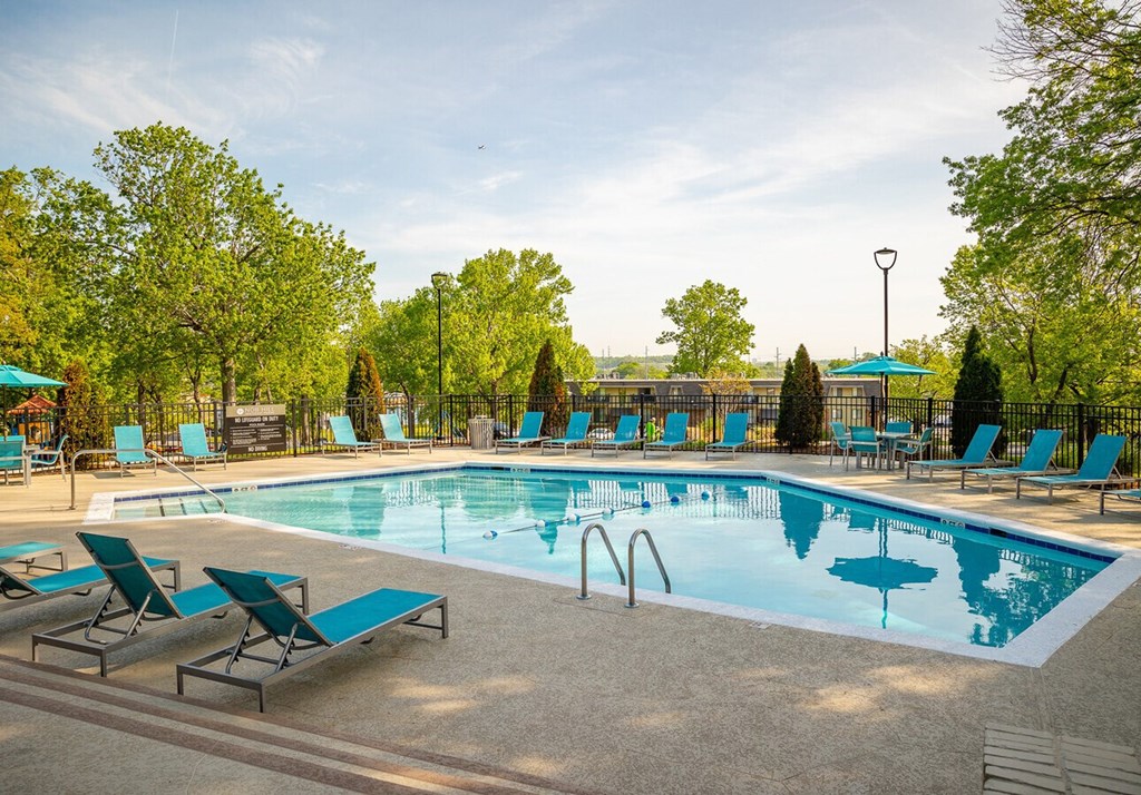 A large outdoor swimming pool surrounded by blue lounge chairs and trees.