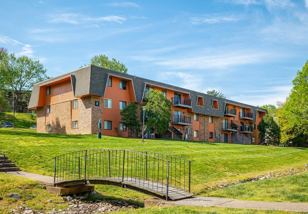 A bridge over a grassy area leads to apartment buildings.