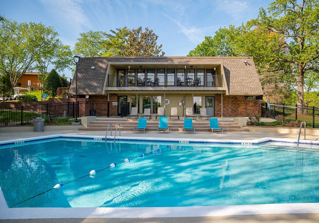 A swimming pool in front of a house with a deck and lounge chairs.