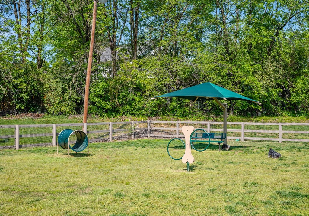 A green umbrella is in a grassy area with a white fence and a green slide.