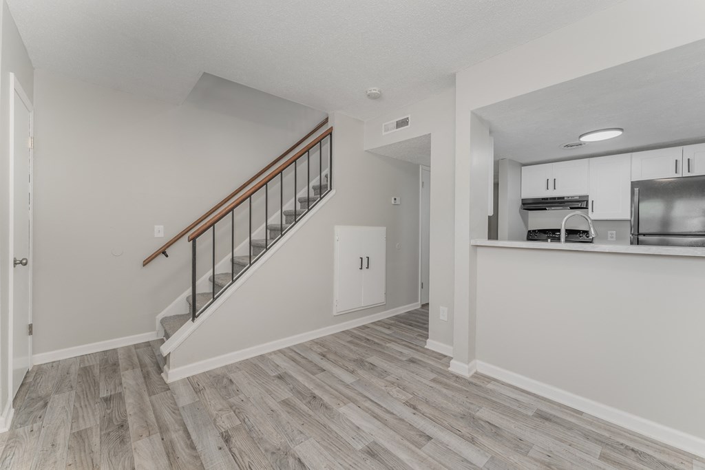 a living room with a staircase and a kitchen in the background