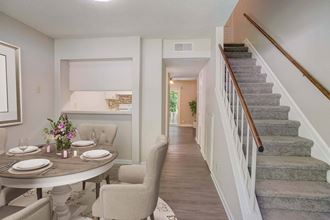 a dining area with a table and chairs and a staircase in the background