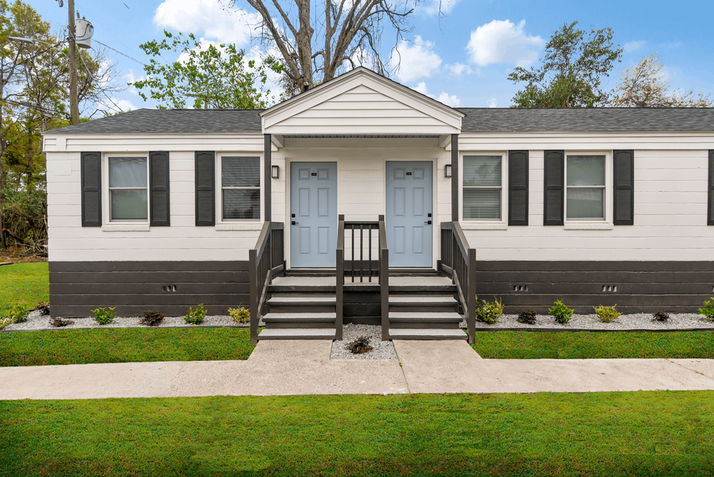 the front of a white house with blue doors and a porch