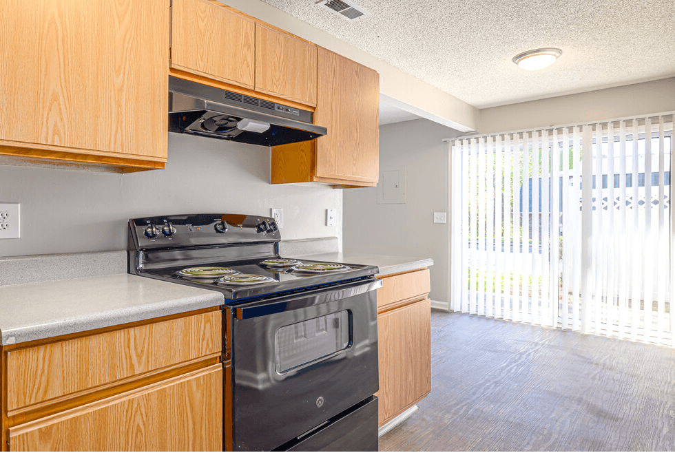an empty kitchen with wood cabinets and an oven and a window
