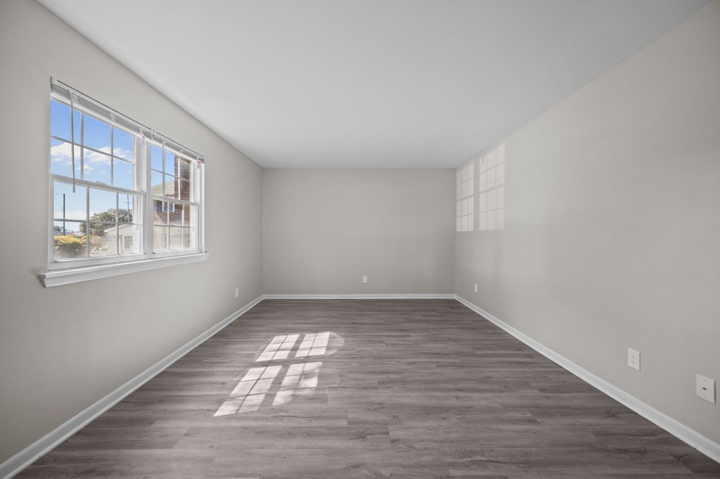 Empty room with a large window and wooden flooring.