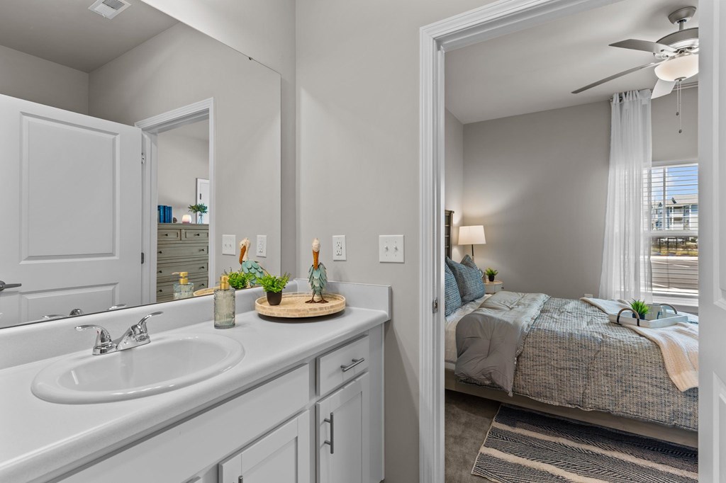 A bathroom with a white sink and a bedroom with a bed and a window.