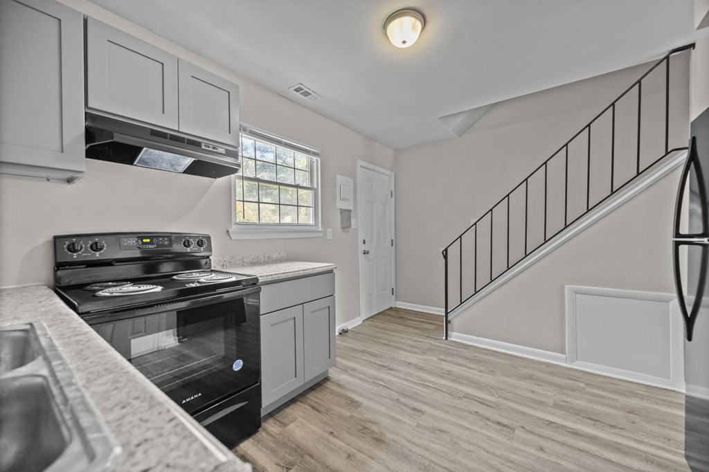 A kitchen with a stove, sink, and a staircase.