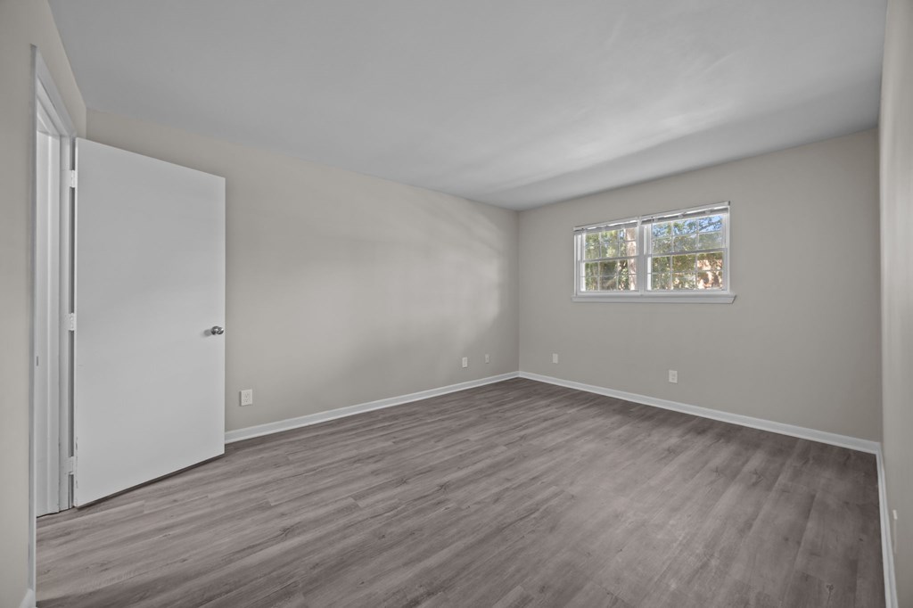 A room with a white door and a window with a view of trees.
