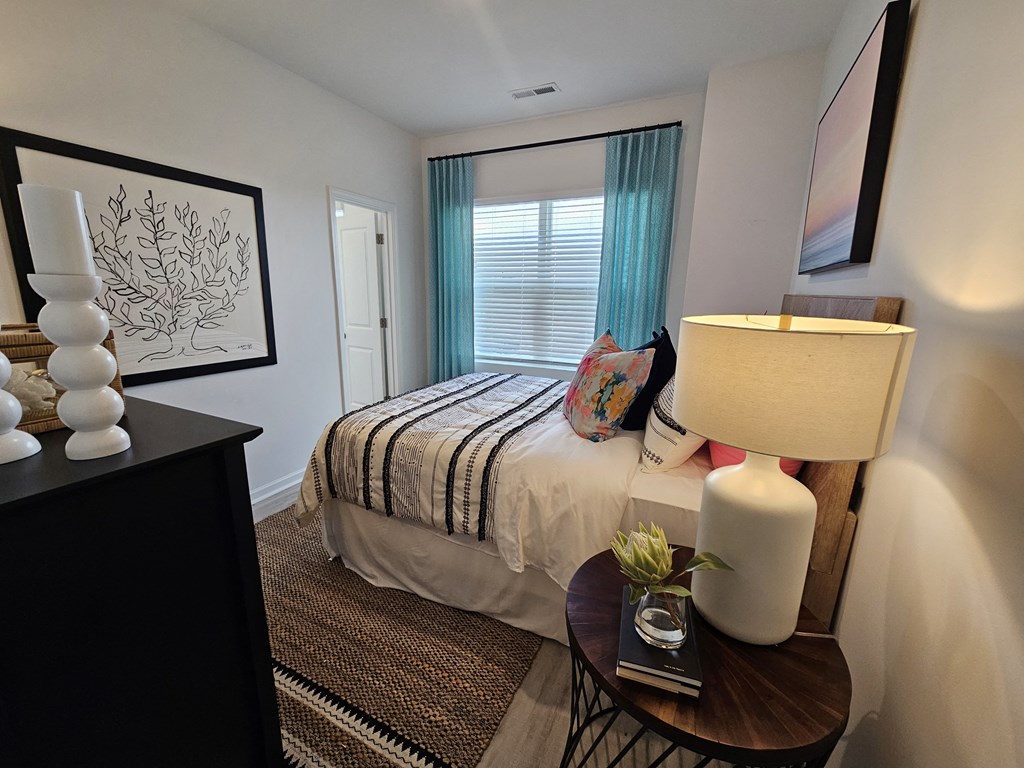 A bedroom with a bed, a nightstand with a lamp, and a small table with a vase of flowers.