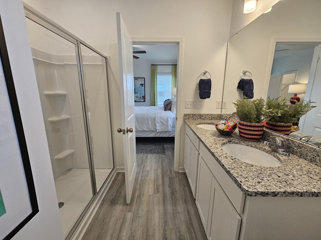 A bathroom with a sink, mirror, and a bed in the background.