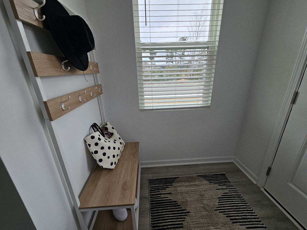 A black hat is hanging on a wooden coat rack next to a white bag with black spots.