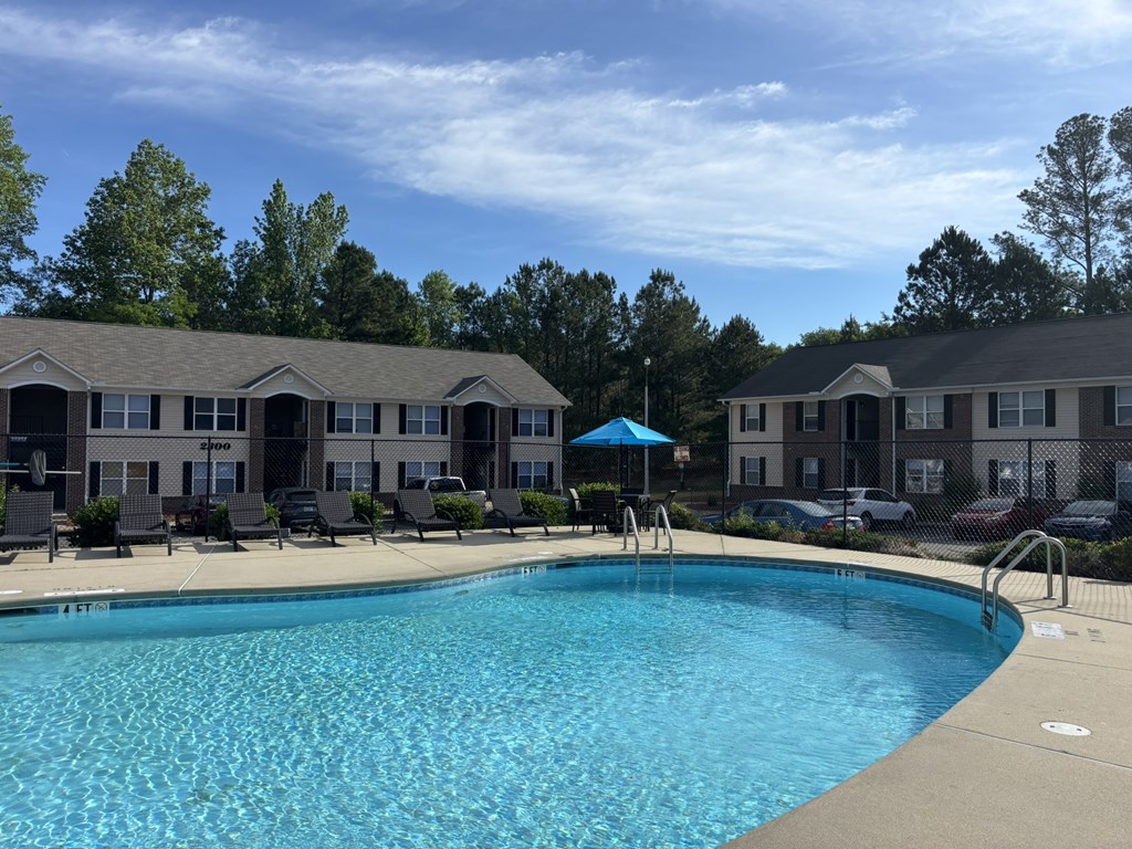 A swimming pool in front of a building with a blue umbrella.