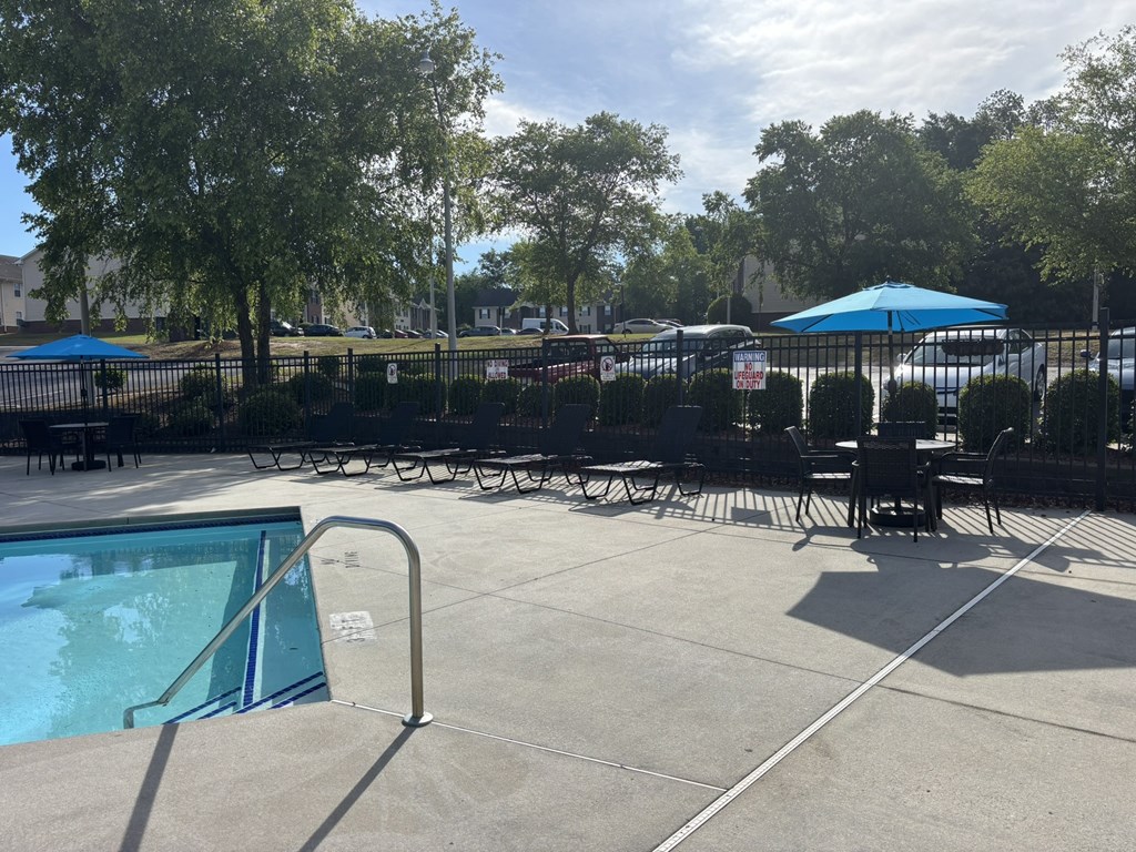 A pool area with a table and chairs and a blue umbrella.