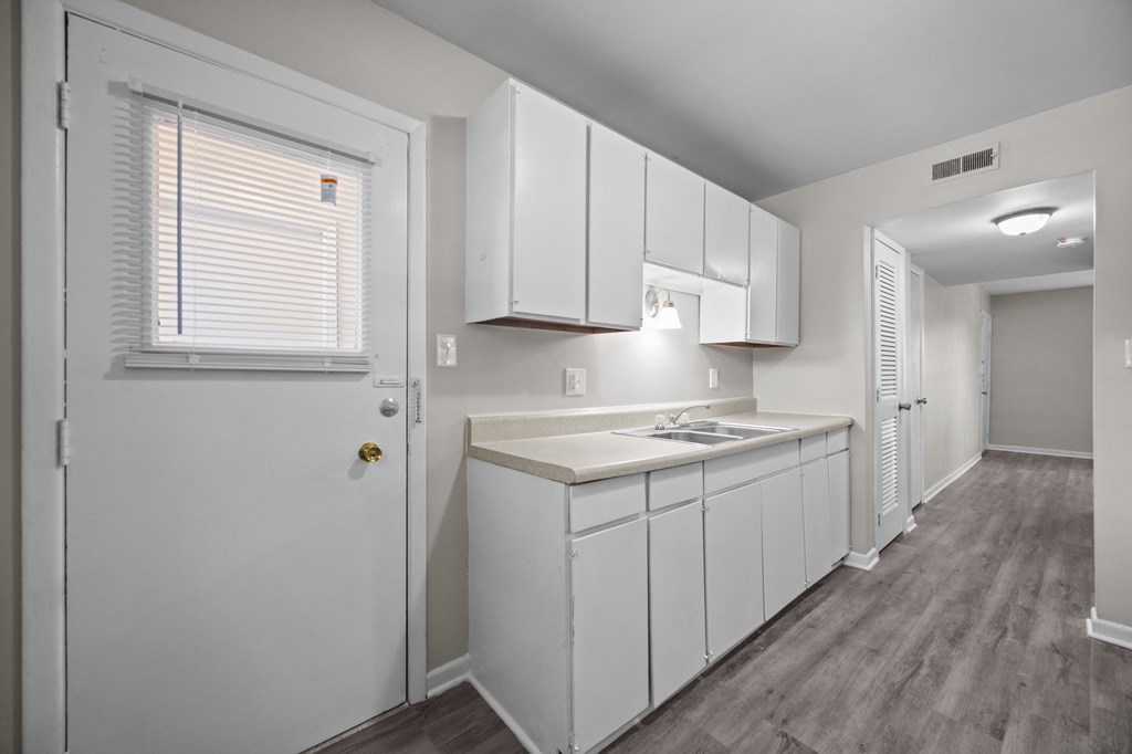 A kitchen with white cabinets and a window with blinds.